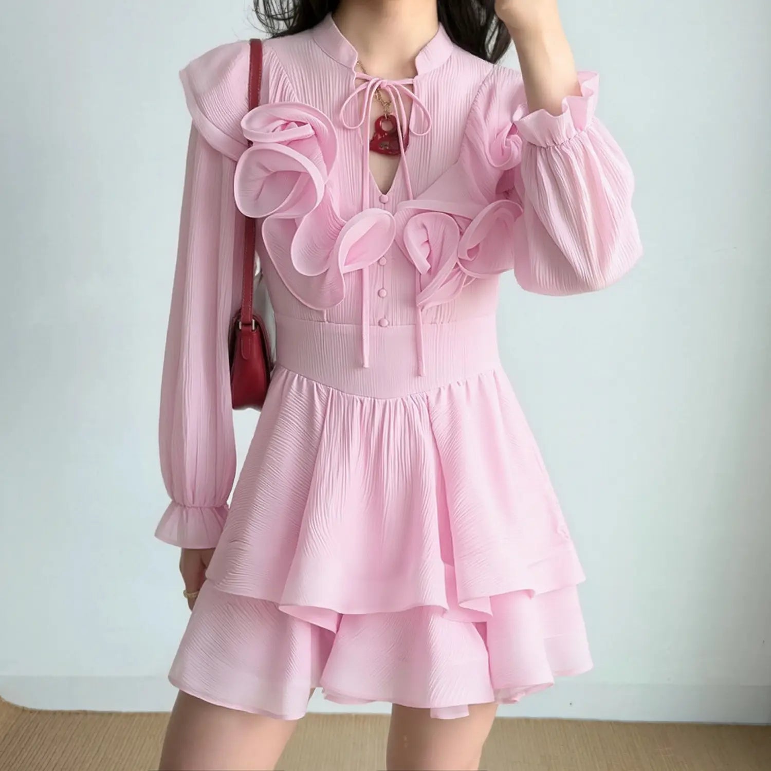 Model wearing light pink stand collar long sleeve mini dress with 3D floral appliques and double-layer ruffle skirt