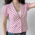 Daily lifestyle model wearing pink polka dot blazer, notched lapel + puff short sleeves, three shell button closure, slim cropped waist fit, matched white inner cami & blue jeans, pearl star pendant necklace styling display