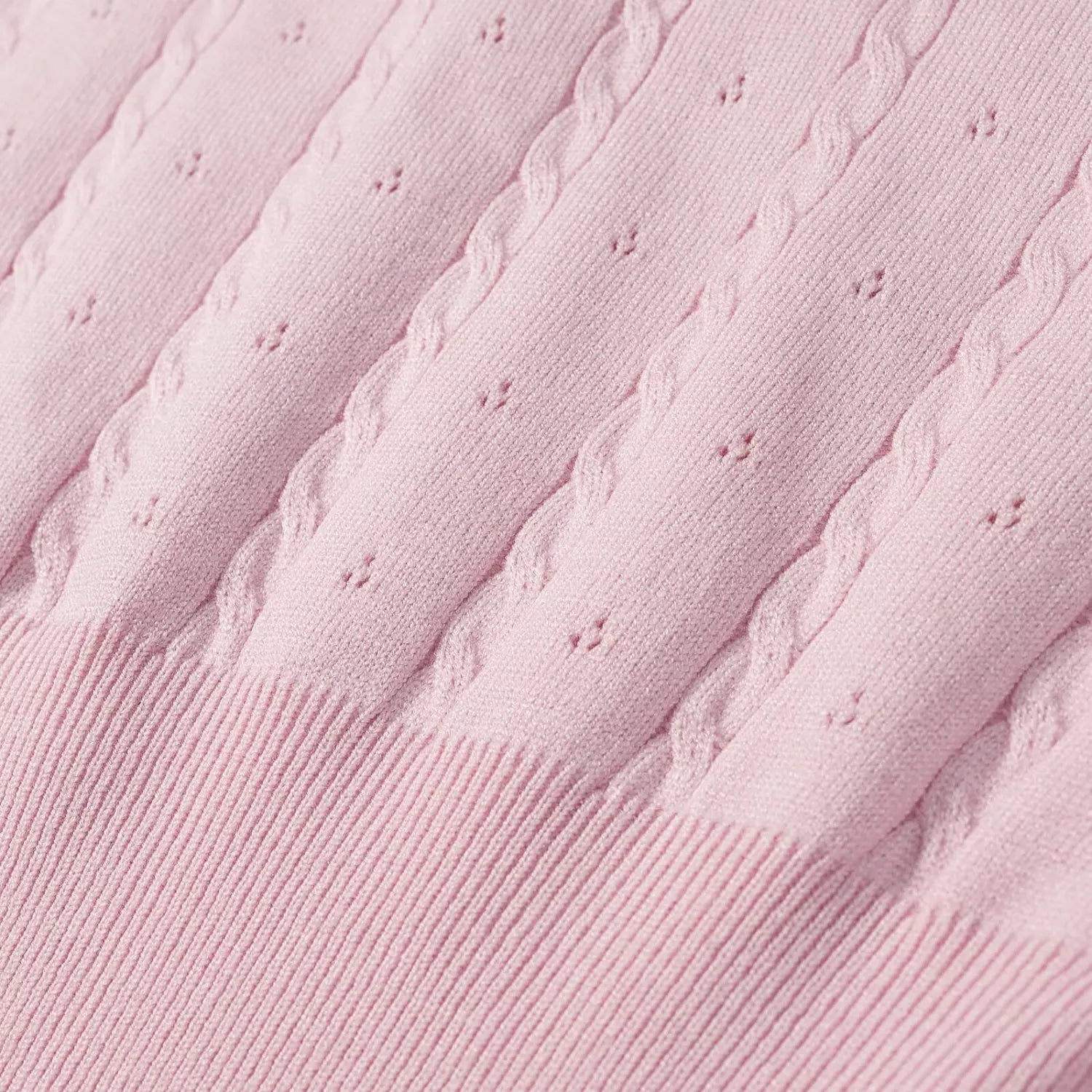 Macro close‑up of pink cable knit fabric, vertical cable stitch and small eyelet perforated texture