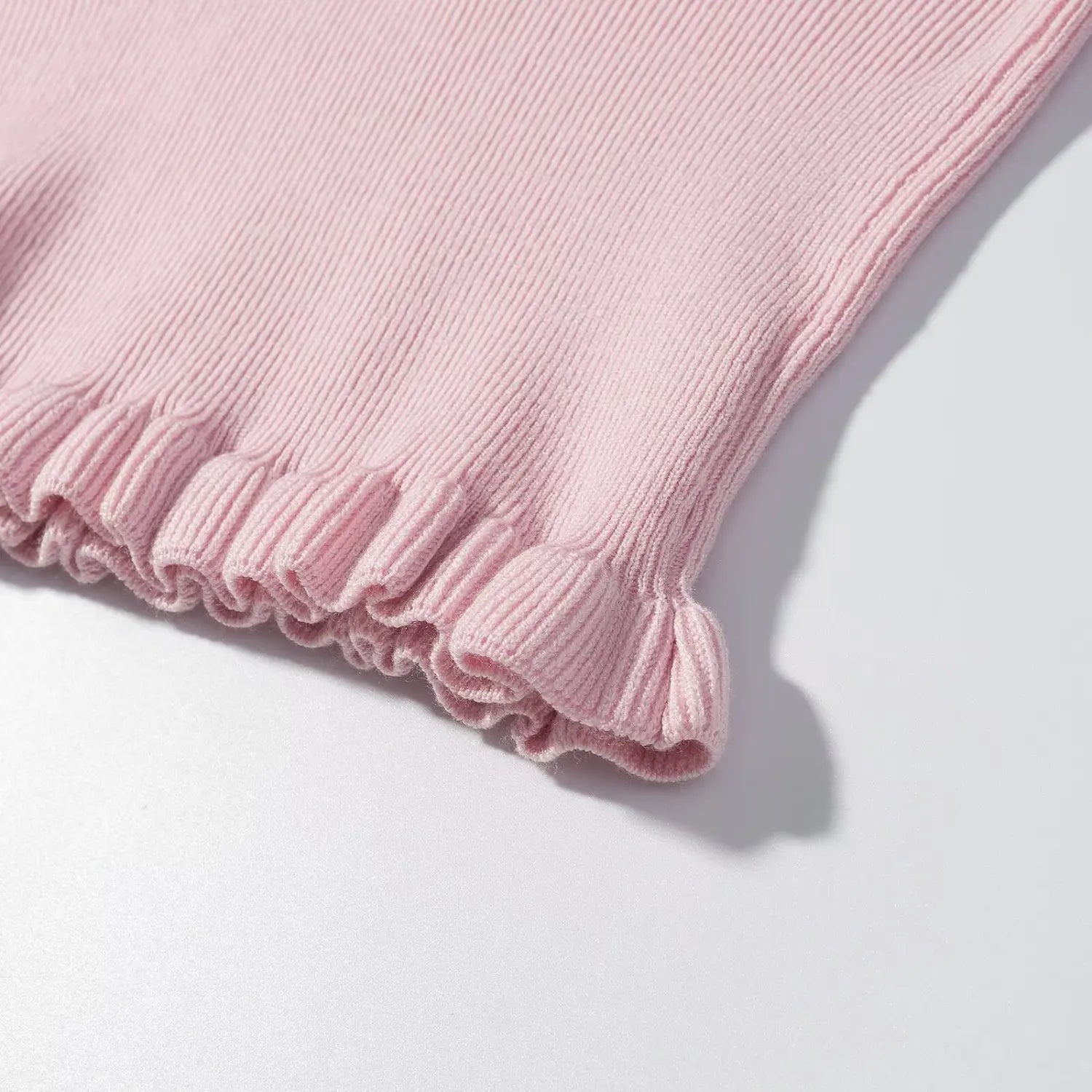 Close‑up of pink cable knit sweater ruffled ribbed hem detail, soft knitted ruffle edge texture