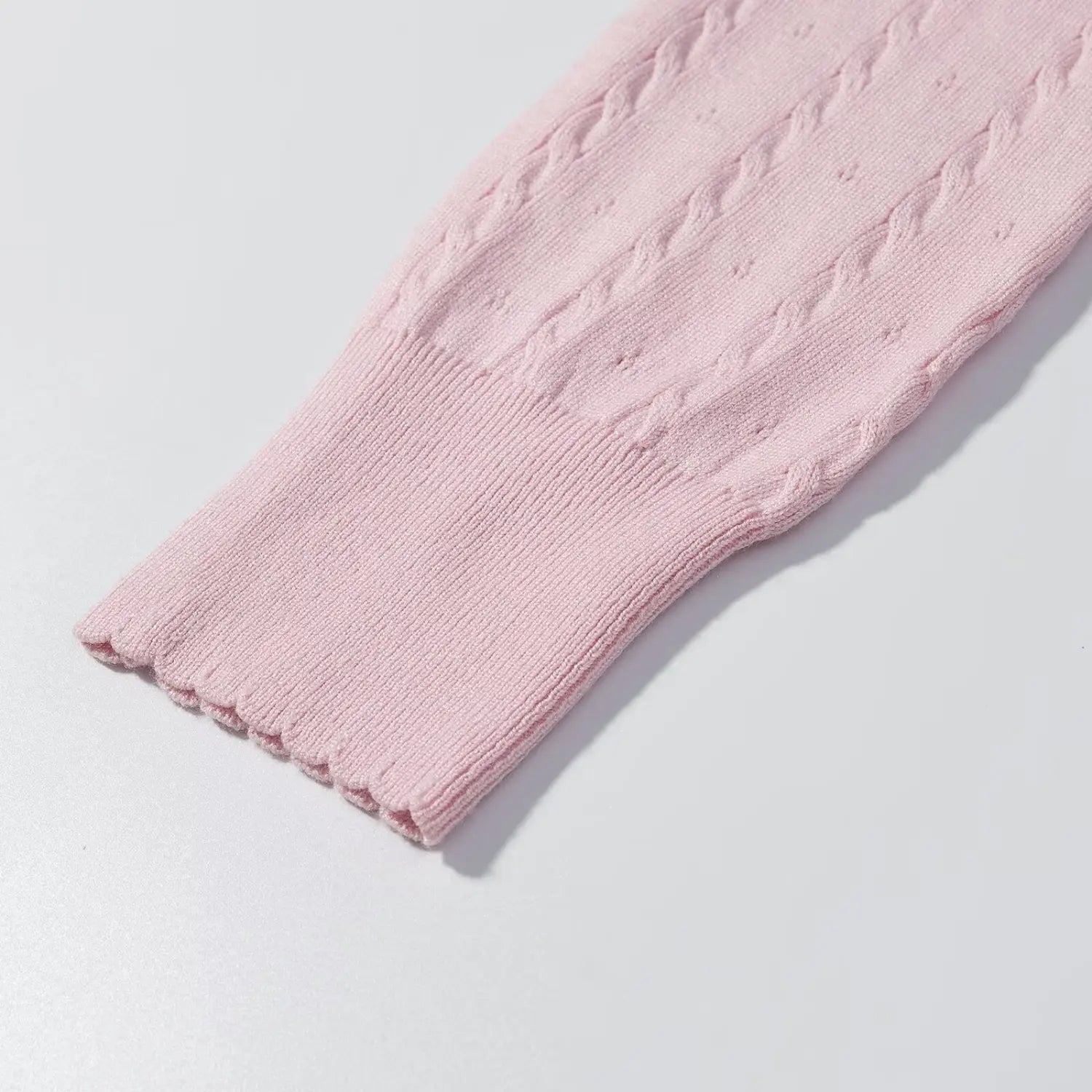 Close‑up of long sleeve scalloped ribbed cuff, pink cable knit eyelet fabric texture