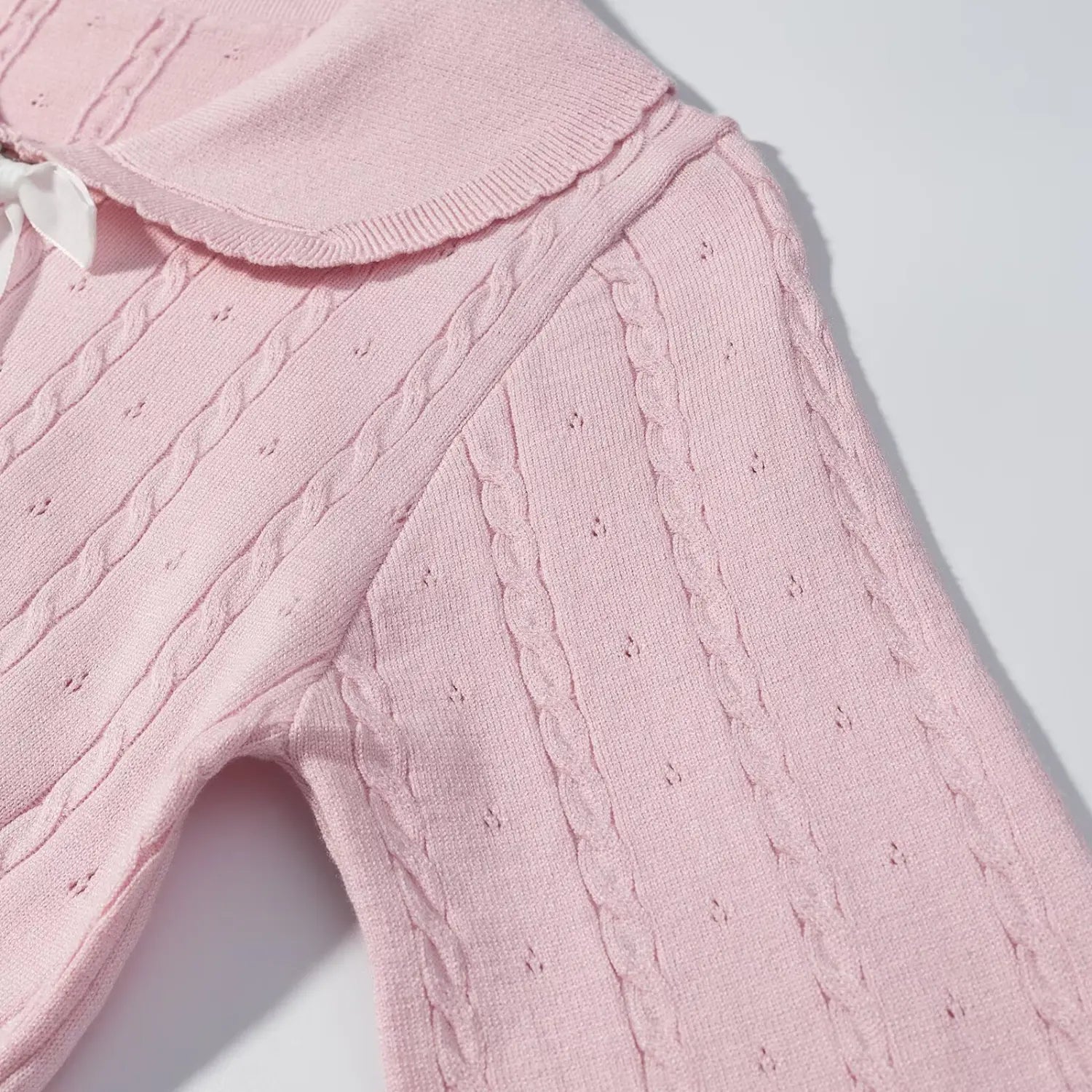 Close‑up of shoulder and sleeve section, pink cable knit sweater with eyelet cable stitch woven texture detail