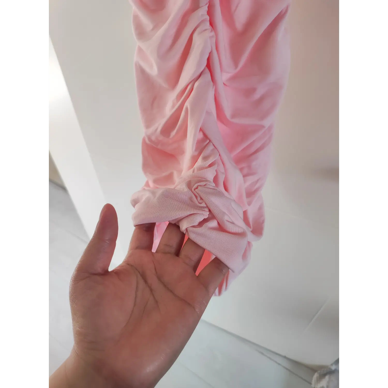 Hand demonstrate adjustable ruched hem drawstring detail of pink stretch mini dress