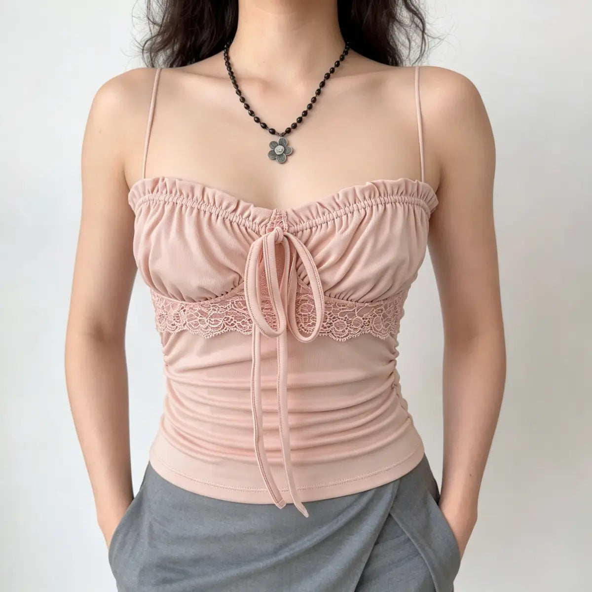 Model with hands in pockets, wearing pink lace-trim cami top and grey bottoms, highlighting the lace waist detail.