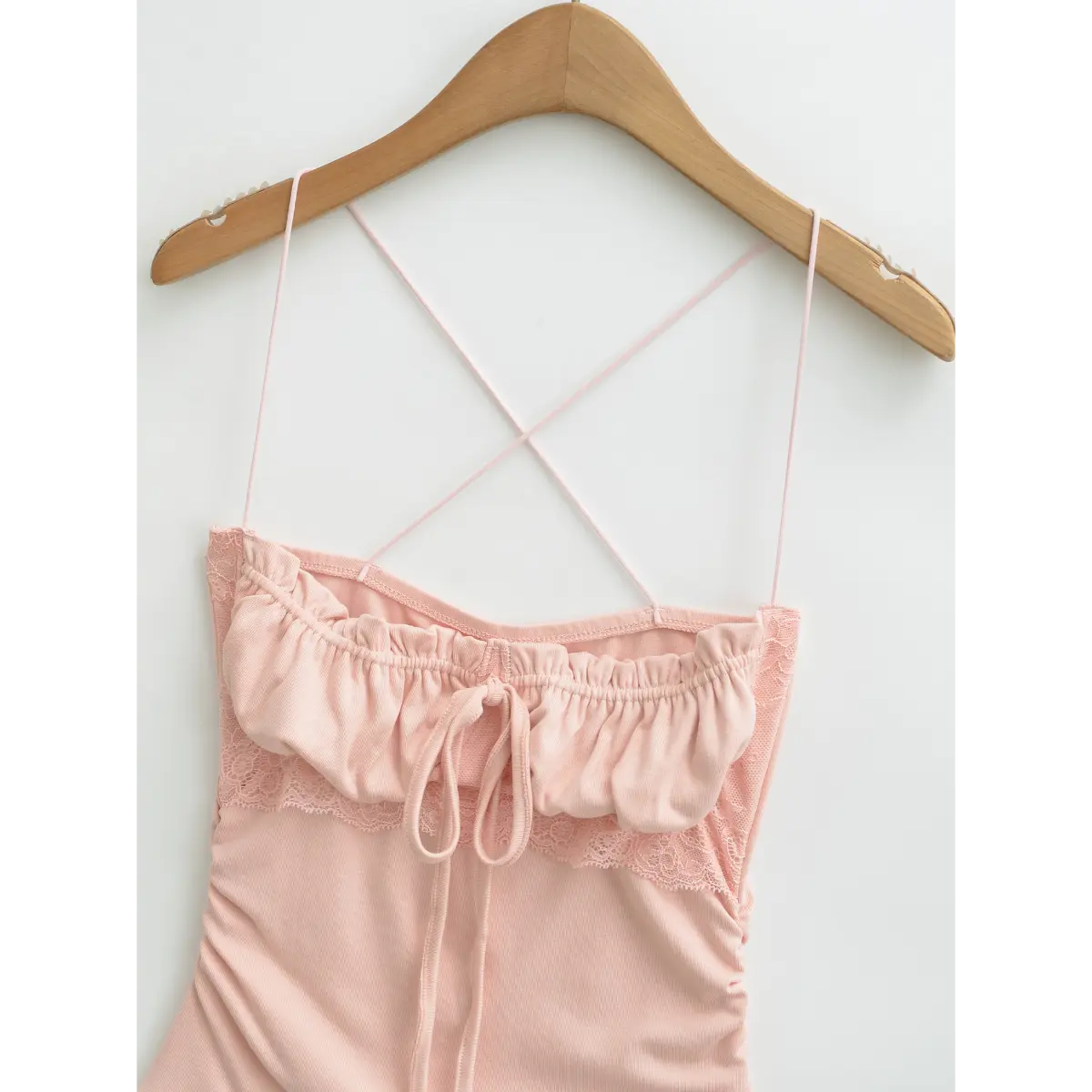Hanger shot of pink cami top, focusing on the lace trim, gathered bust and crisscross strap design.