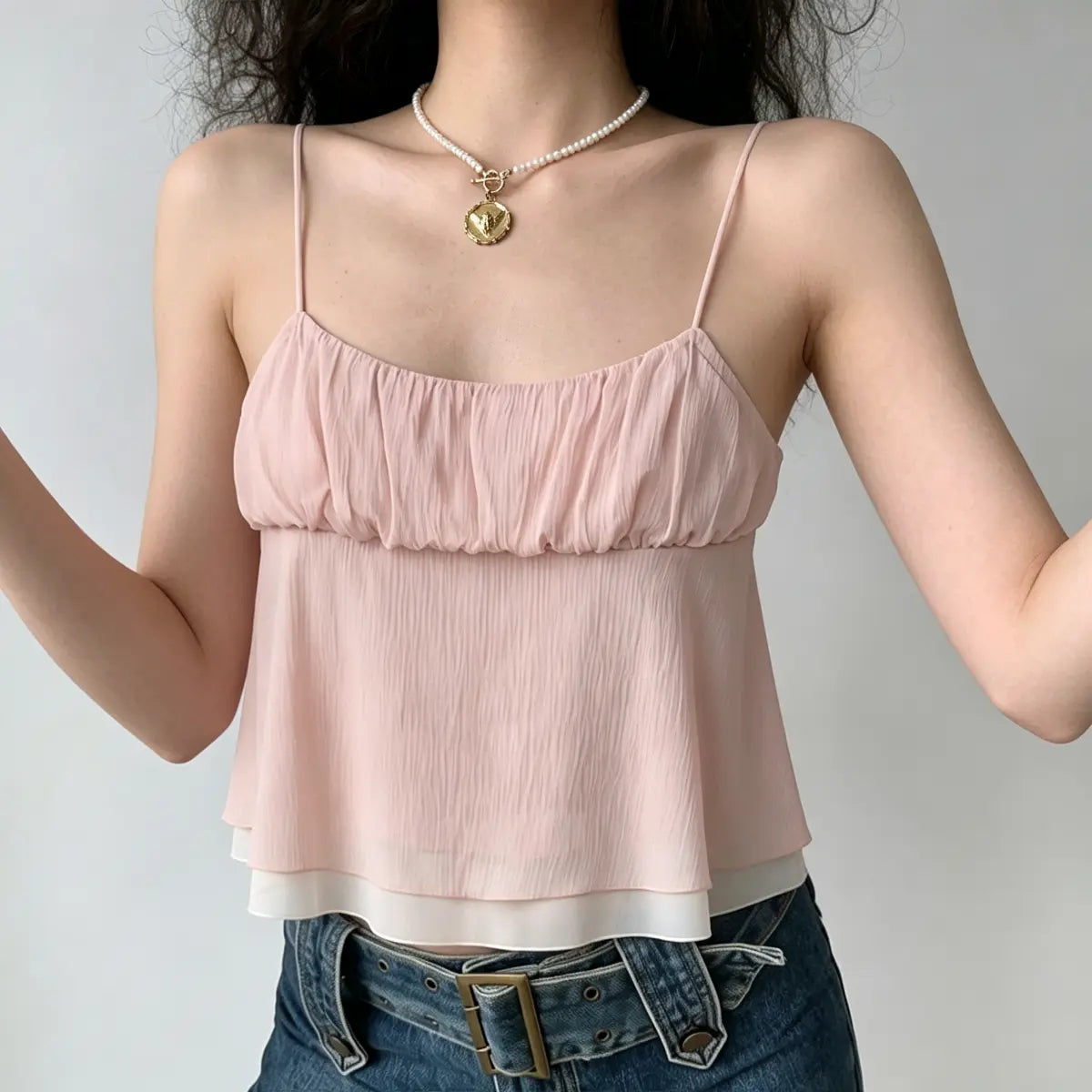 Model with hands raised, wearing a light pink double-layer ruffled cami top, highlighting the flowy silhouette and sheer underlayer.