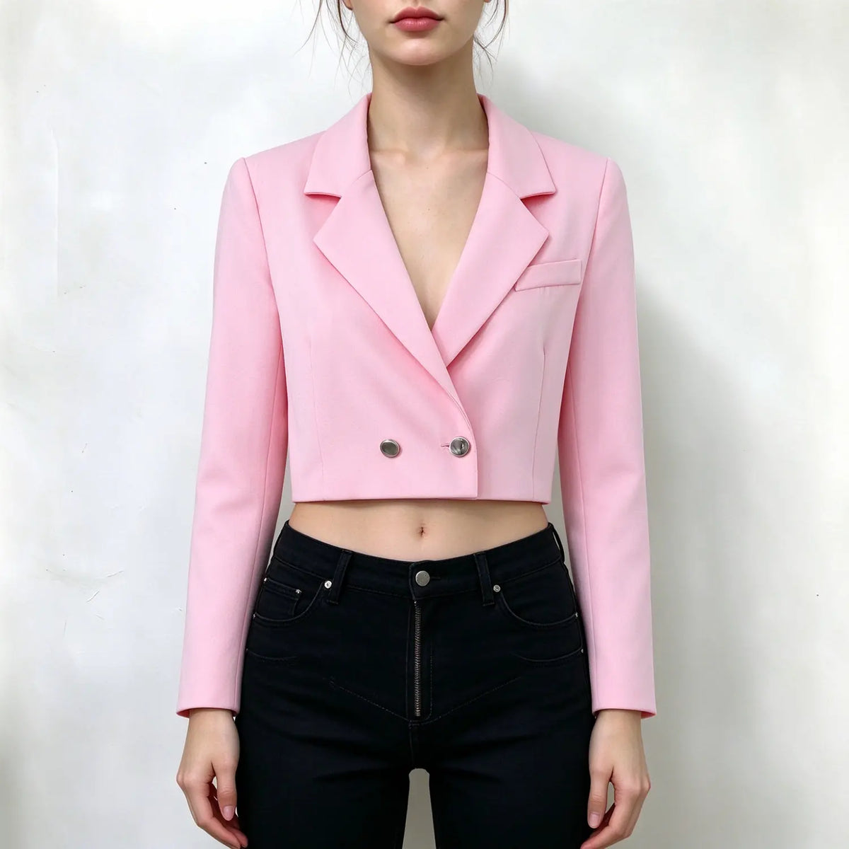 Model wearing pink cropped blazer, notched lapel, double silver button closure, long sleeves, cropped length, paired with black jeans, plain white background