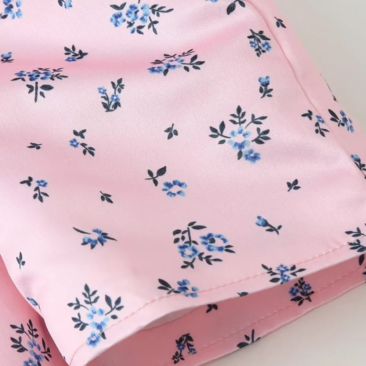 Close-up of the hem on the pink ditsy floral blouse, showing the smooth fabric and small blue flower print