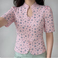 The pink ditsy floral blouse worn by a model, showing the fitted silhouette, keyhole neckline, and puff sleeves