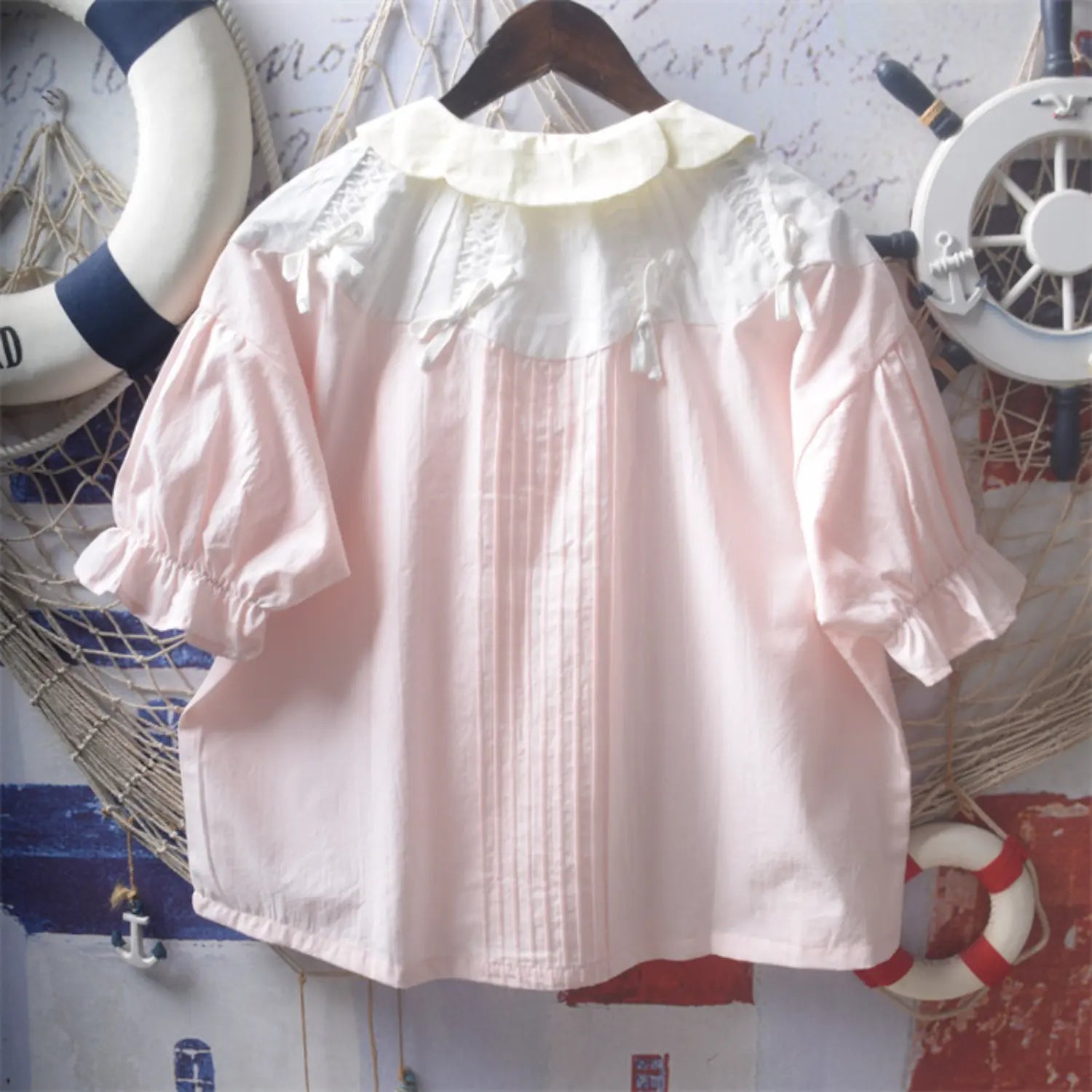 Light pink doll collar blouse full back hanging flat shot, full spliced ruffle collar symmetrical shoulder bows full back vertical pleated tucks loose dropped shoulder silhouette back simple soft style display