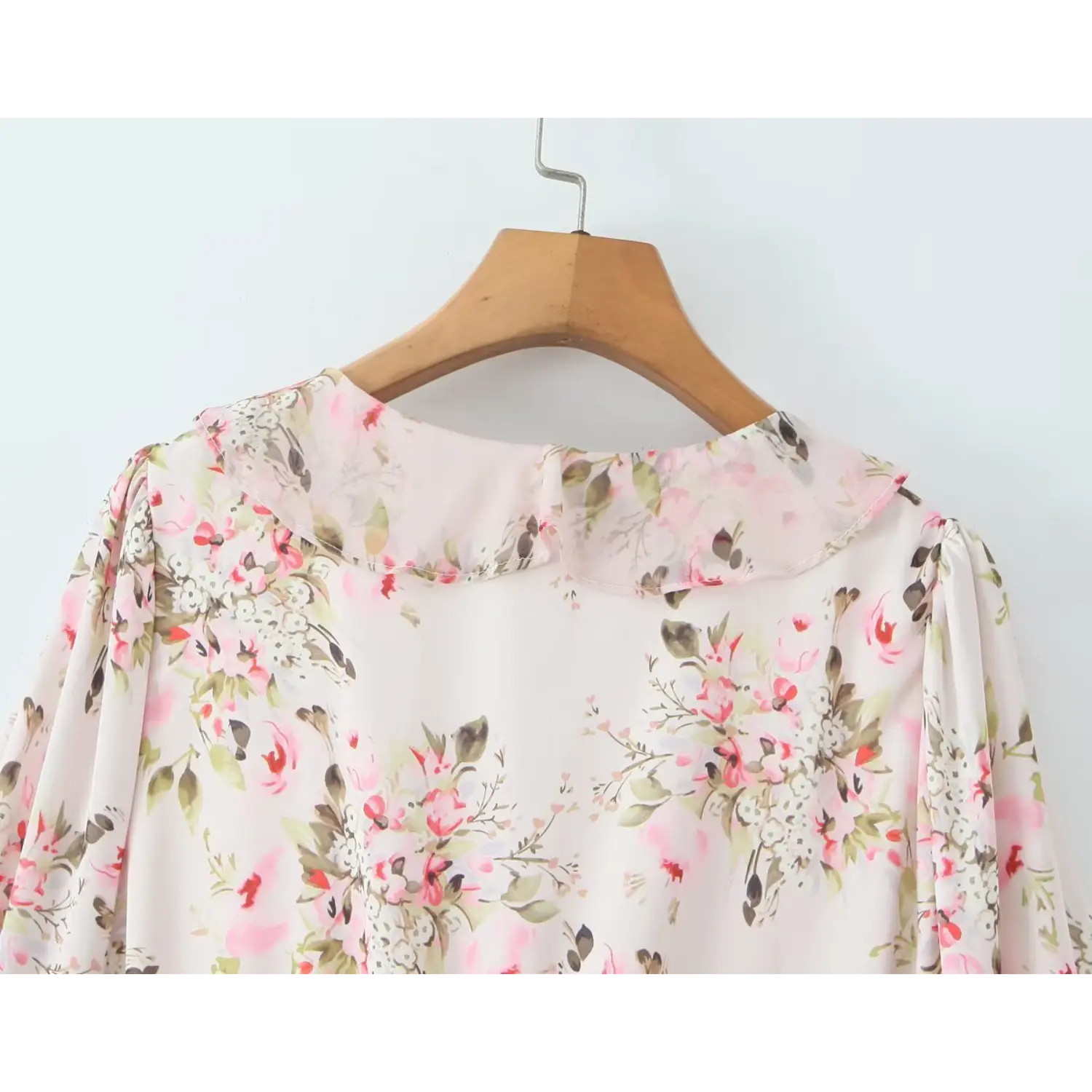 Close‑up back ruffle collar detail of pink floral long sleeve chiffon mini dress on wooden hanger