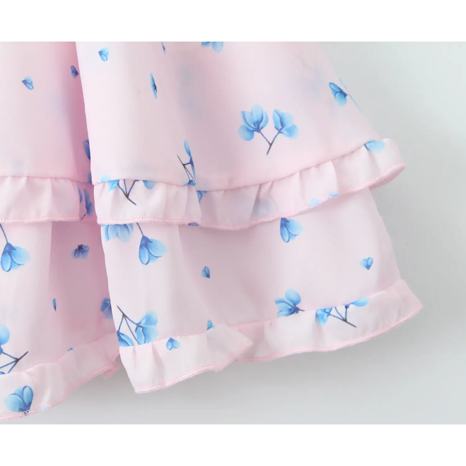Close‑up of double tier ruffle hem, frilled trim edge, pale pink fabric with scattered blue floral print, lightweight flowy chiffon