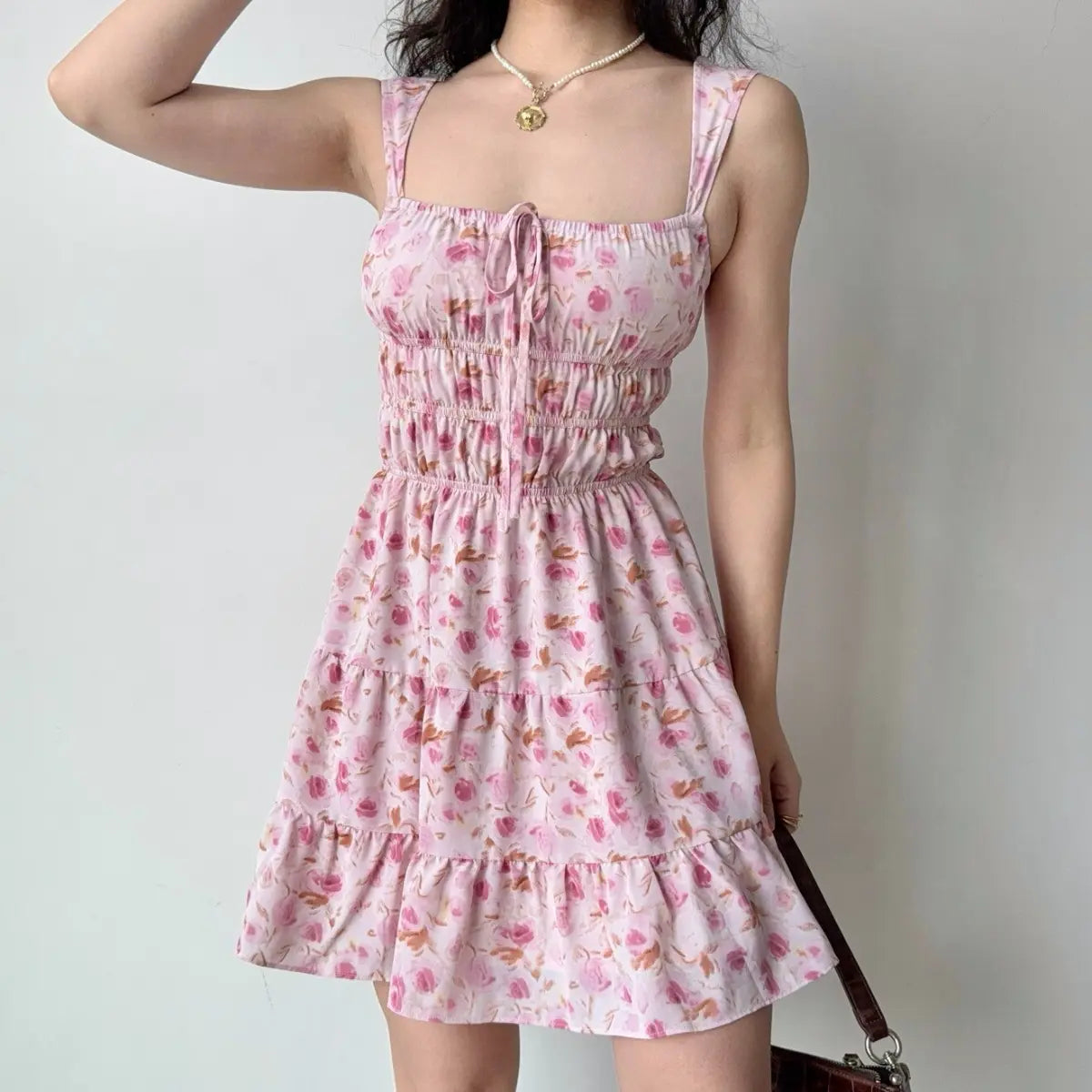 The pink floral tiered dress styled with a brown crocodile-pattern shoulder bag.