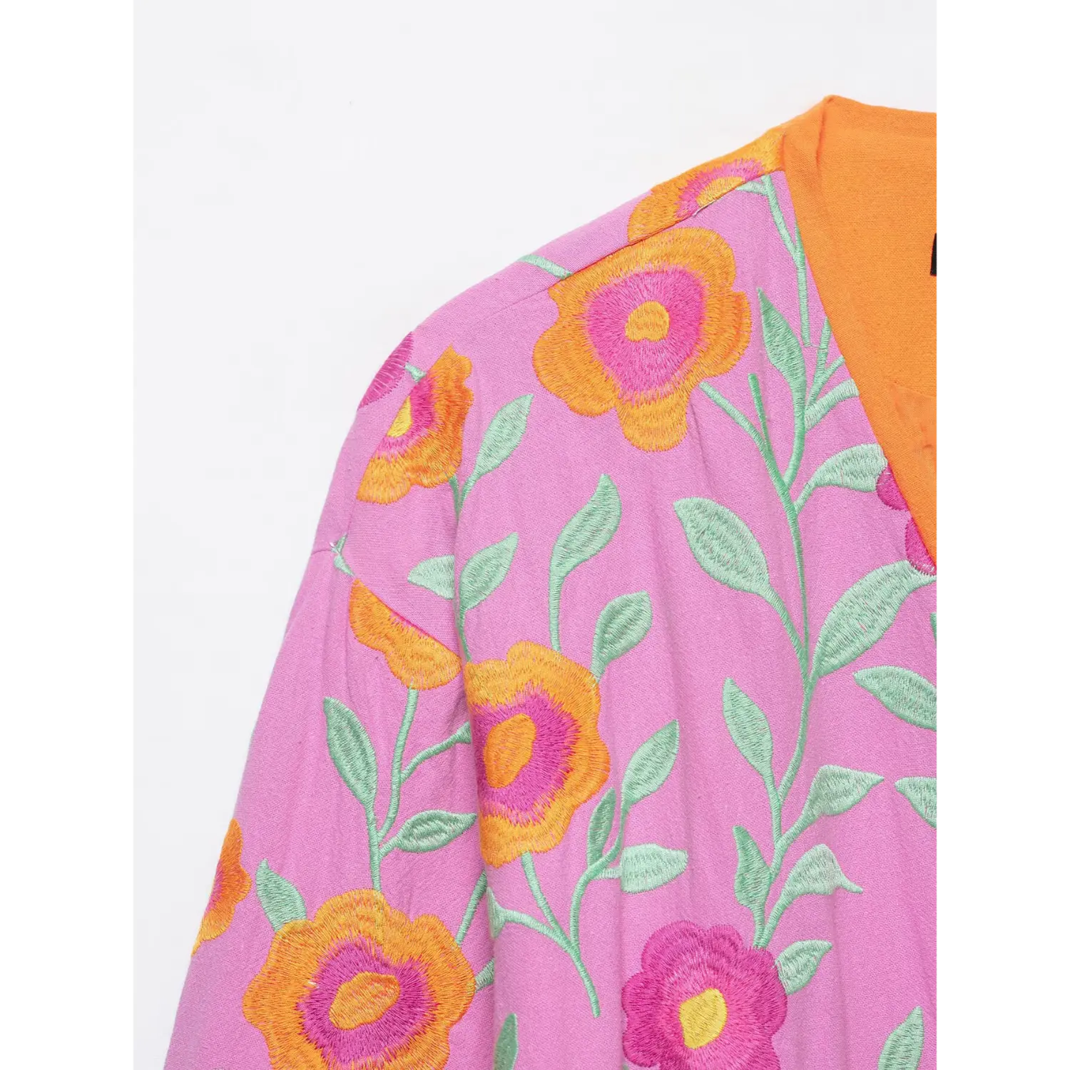 Close up of colorful floral embroidery on pink boho wrap jacket shoulder, green leaf stitching detail