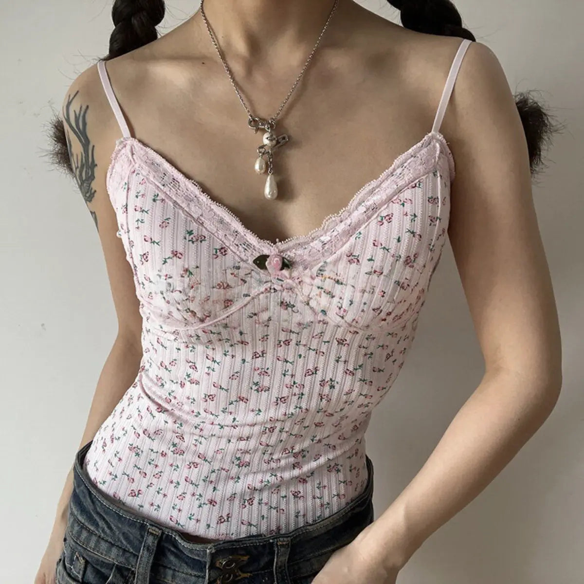A woman wearing a pink floral lace-trimmed cami top with denim jeans, accessorized with a pearl necklace.