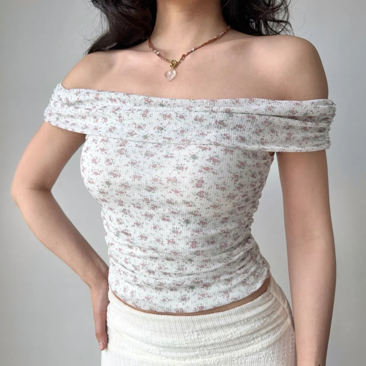 Woman wearing a pink floral off-shoulder top, accessorized with a heart necklace, highlighting the ribbed texture and form-fitting silhouette.
