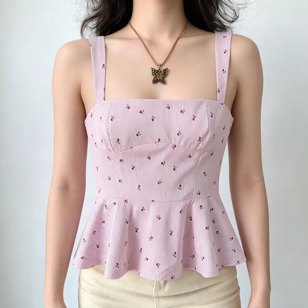 Full front view of a light pink floral peplum cami top, showing the wide straps, square neckline, and flared peplum hem.