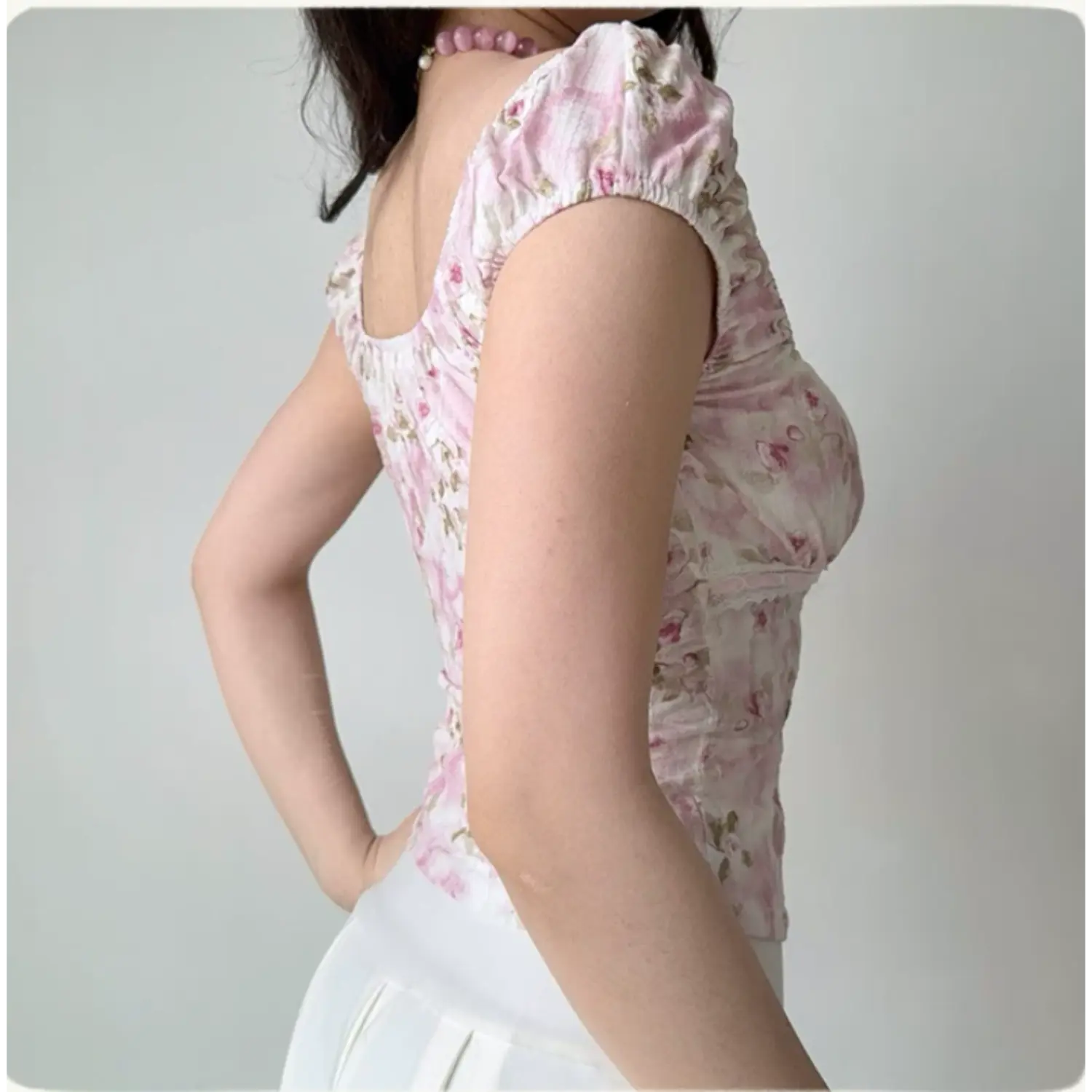 Lifestyle back shot of a woman wearing a pink floral square-neck top with puff sleeves, paired with a white skirt
