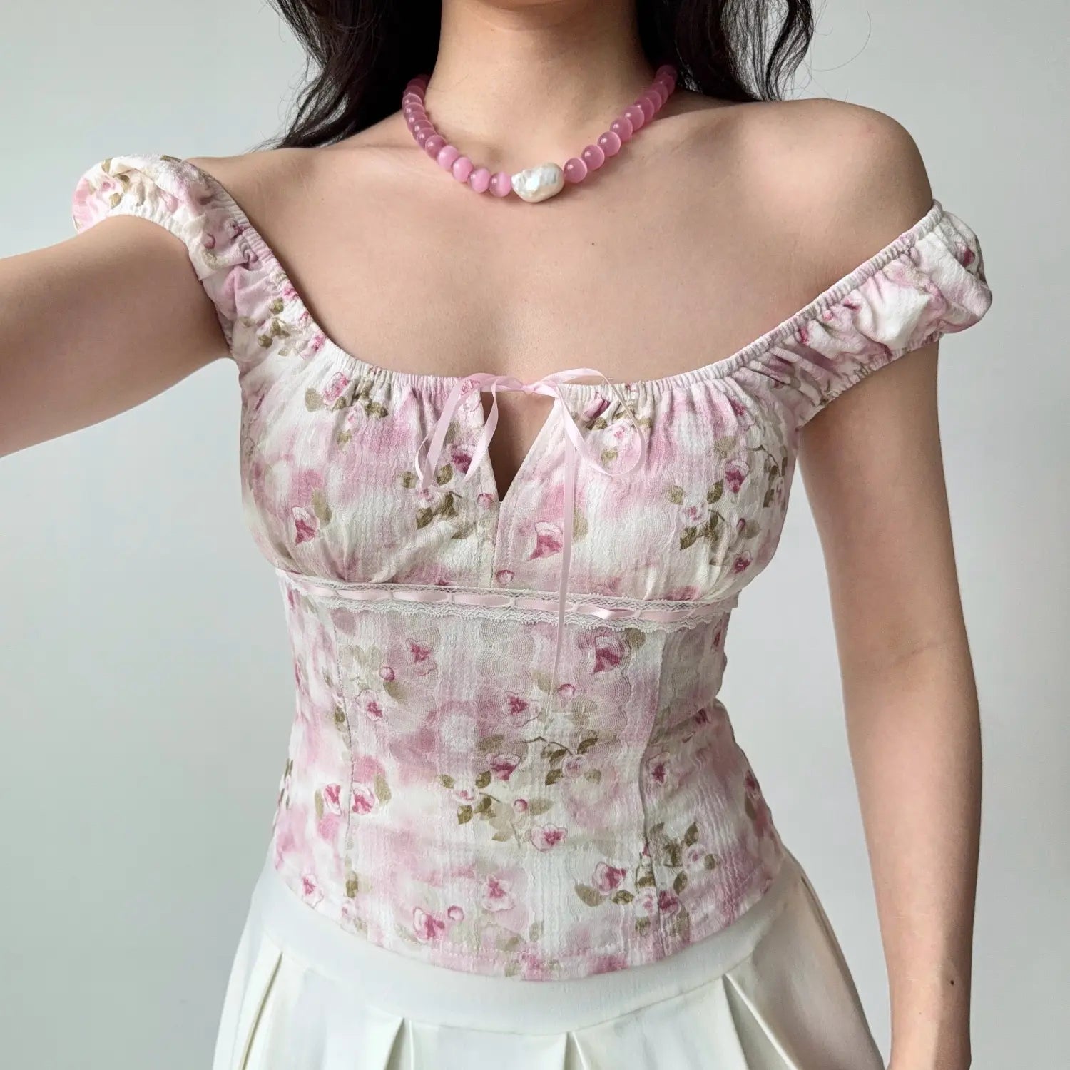 Selfie shot of a woman in a pink floral square-neck top, with one arm raised to frame the shot