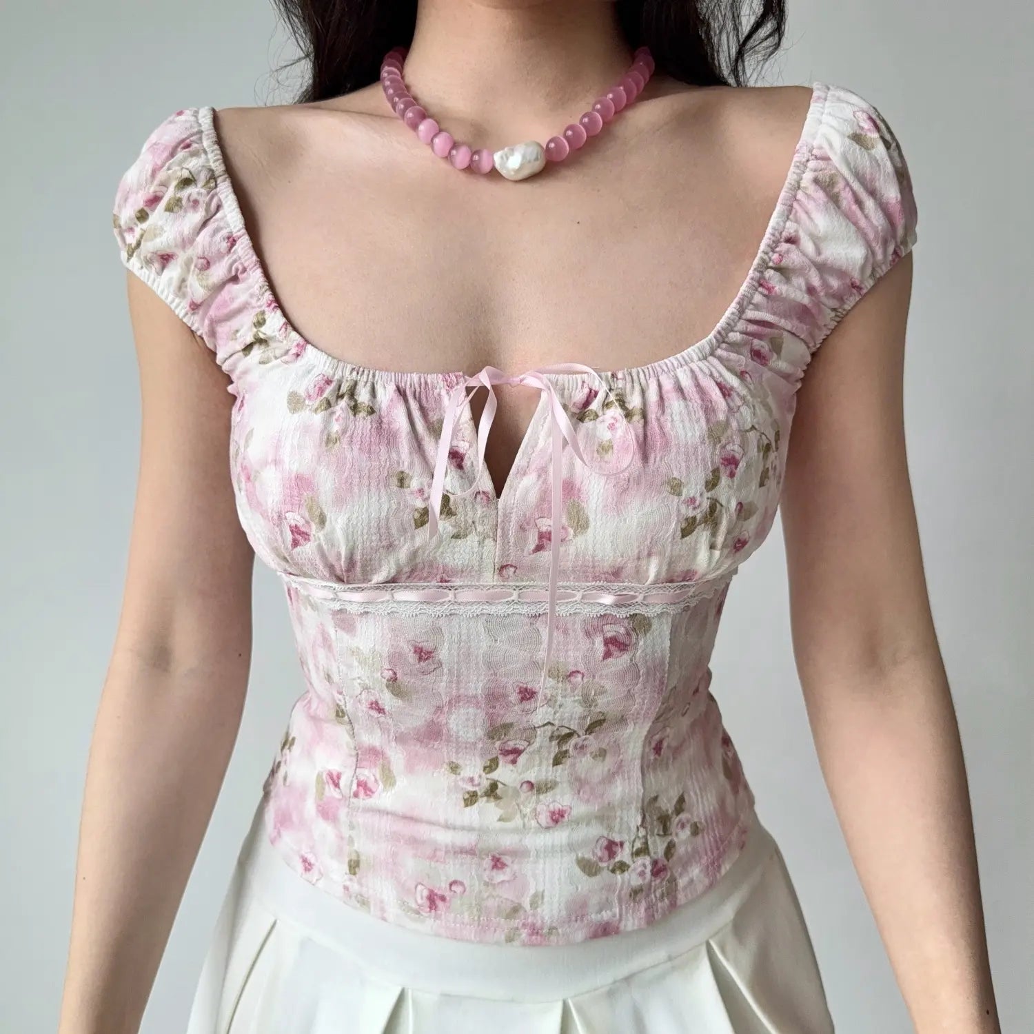  Lifestyle shot of a woman in a pink floral square-neck top, showing the front tie detail and lace trim at the waist