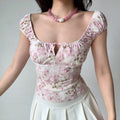 Full-body shot of a woman in a pink floral square-neck top, standing with arms relaxed at her sides