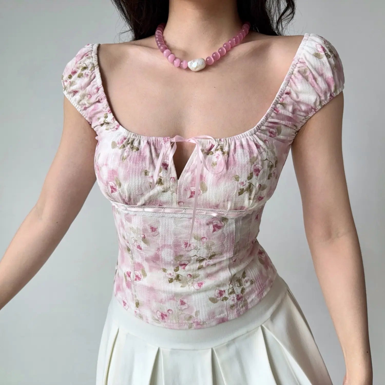 Full-body shot of a woman in a pink floral square-neck top, standing with arms relaxed at her sides