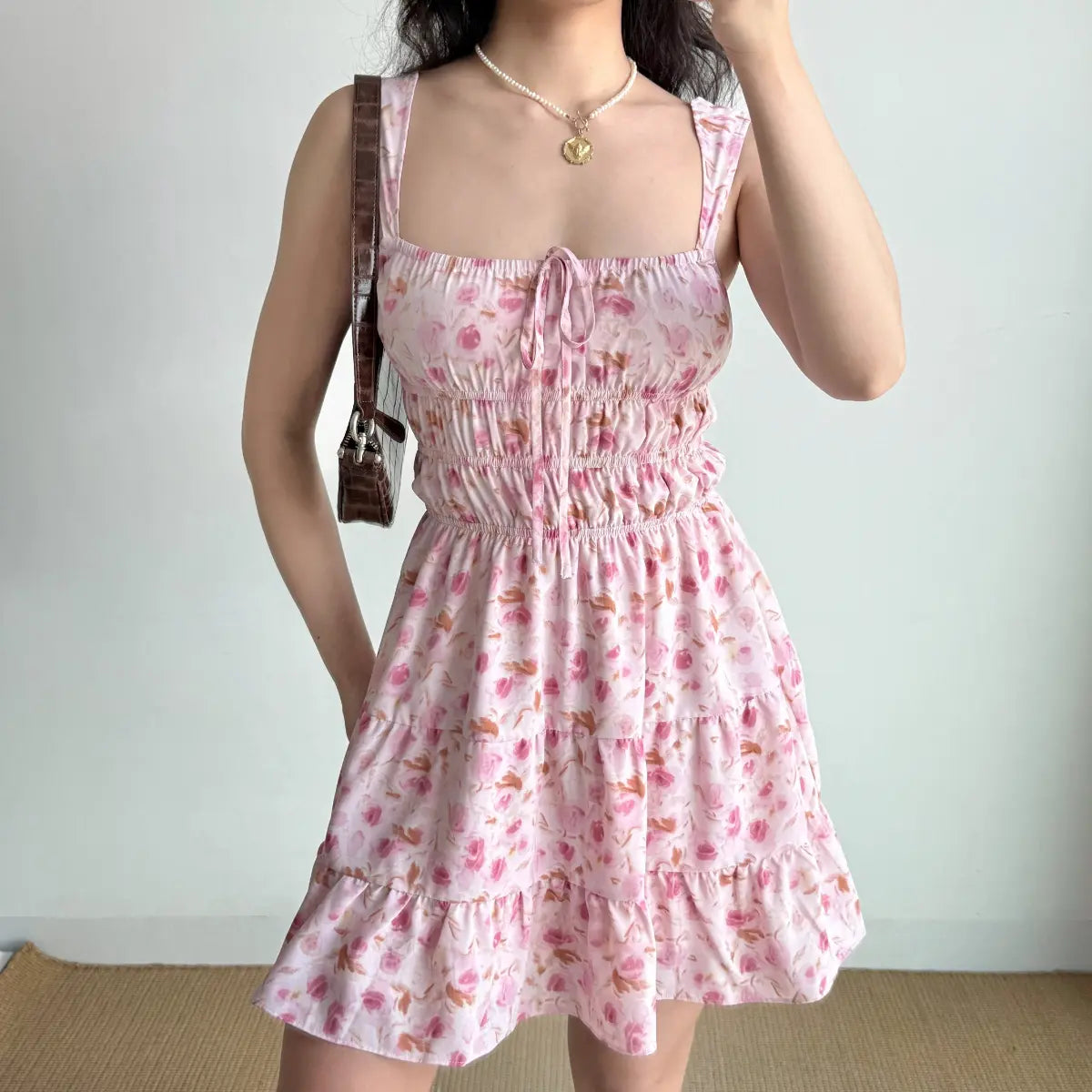 Front view of a pink floral tiered mini dress with a smocked waist and tie detail.