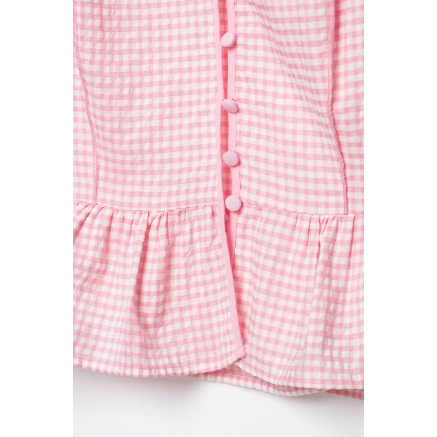 Macro close-up of front fabric button placket and ruffled peplum hem, light pink white gingham crinkle woven fabric