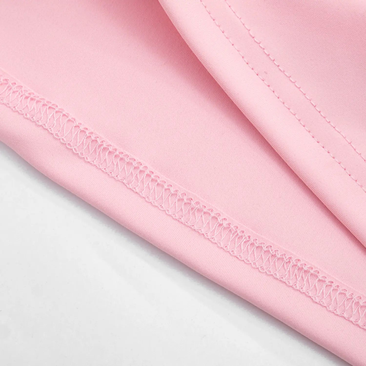 Texture macro close-up of tank top bottom hem, baby pink stretch knit fabric with matching pink wavy elastic overlock stitching, double folded hem for durability and smooth drape
