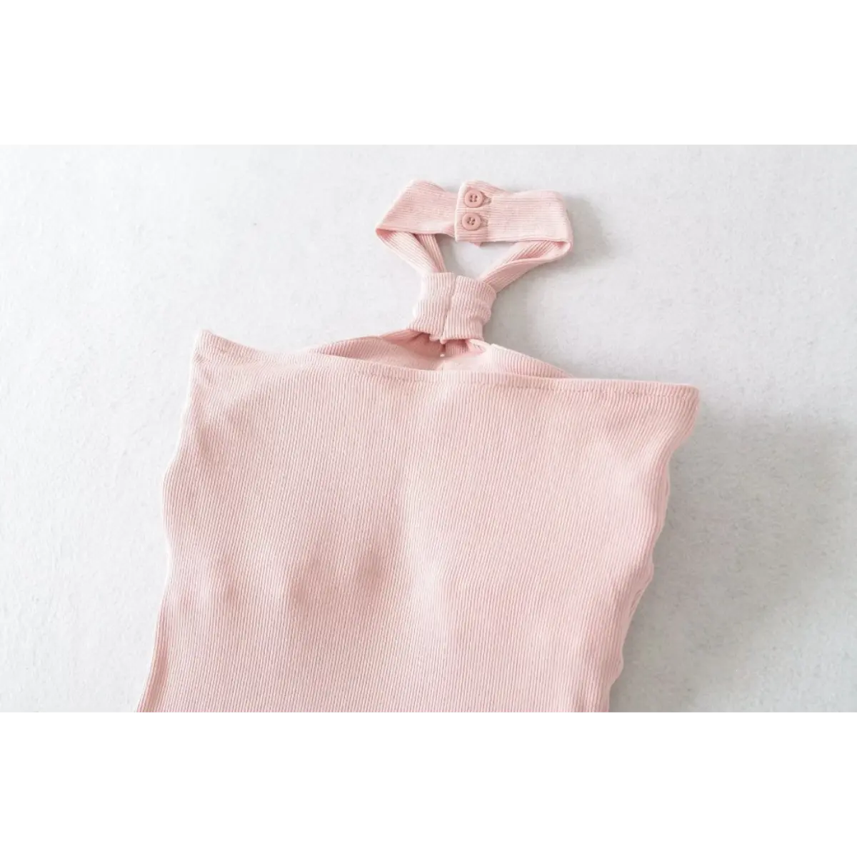 Back view of a pink ribbed halter top, showing the button closure at the neck.