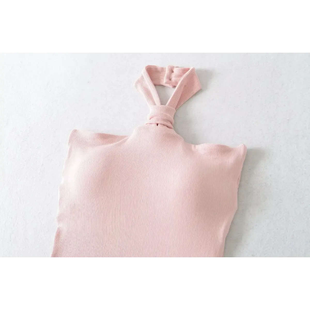 Flat lay view of a pink ribbed halter top, showing the front knot detail and button closure at the neck.