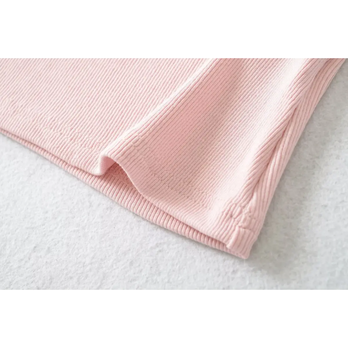 Close-up of the hem on a pink ribbed halter top, showing the fine vertical texture and stitching.
