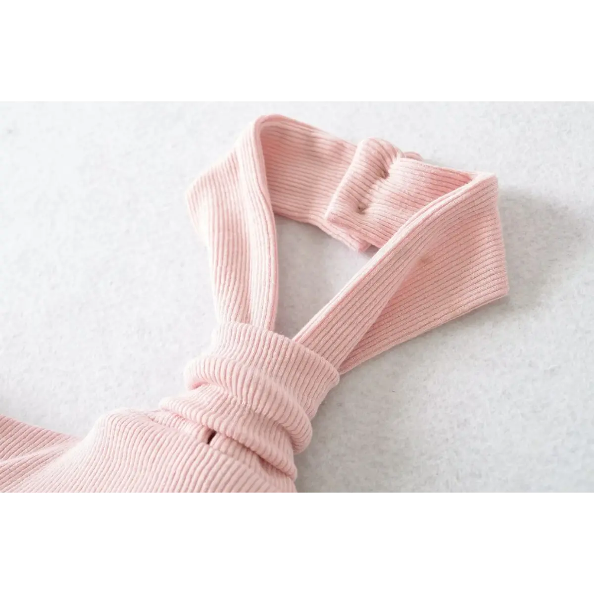 Close-up of the neckline and knot detail on a pink ribbed halter top, showing the button closure.

