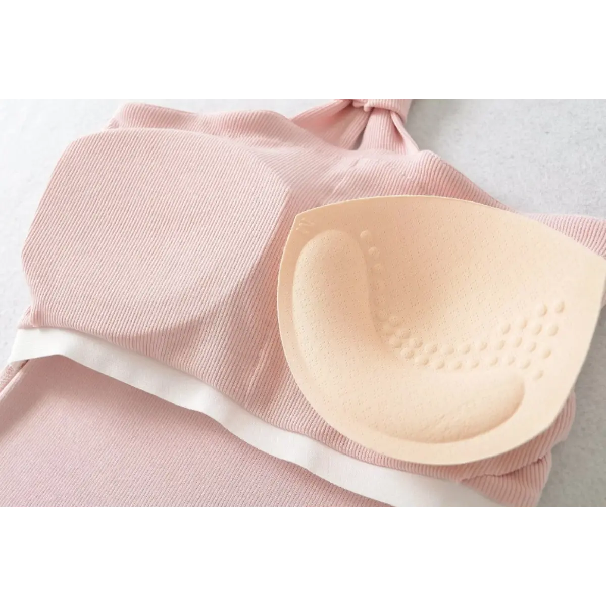 Close-up of a pink ribbed halter top with a removable molded bra pad, showing the perforated texture of the pad.
