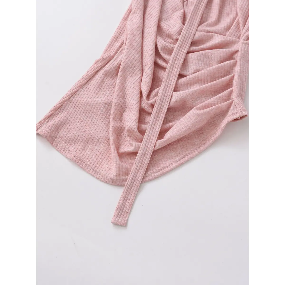 Close-up of the asymmetric hem on a pink ribbed halter wrap top, showing the texture and tie strap.