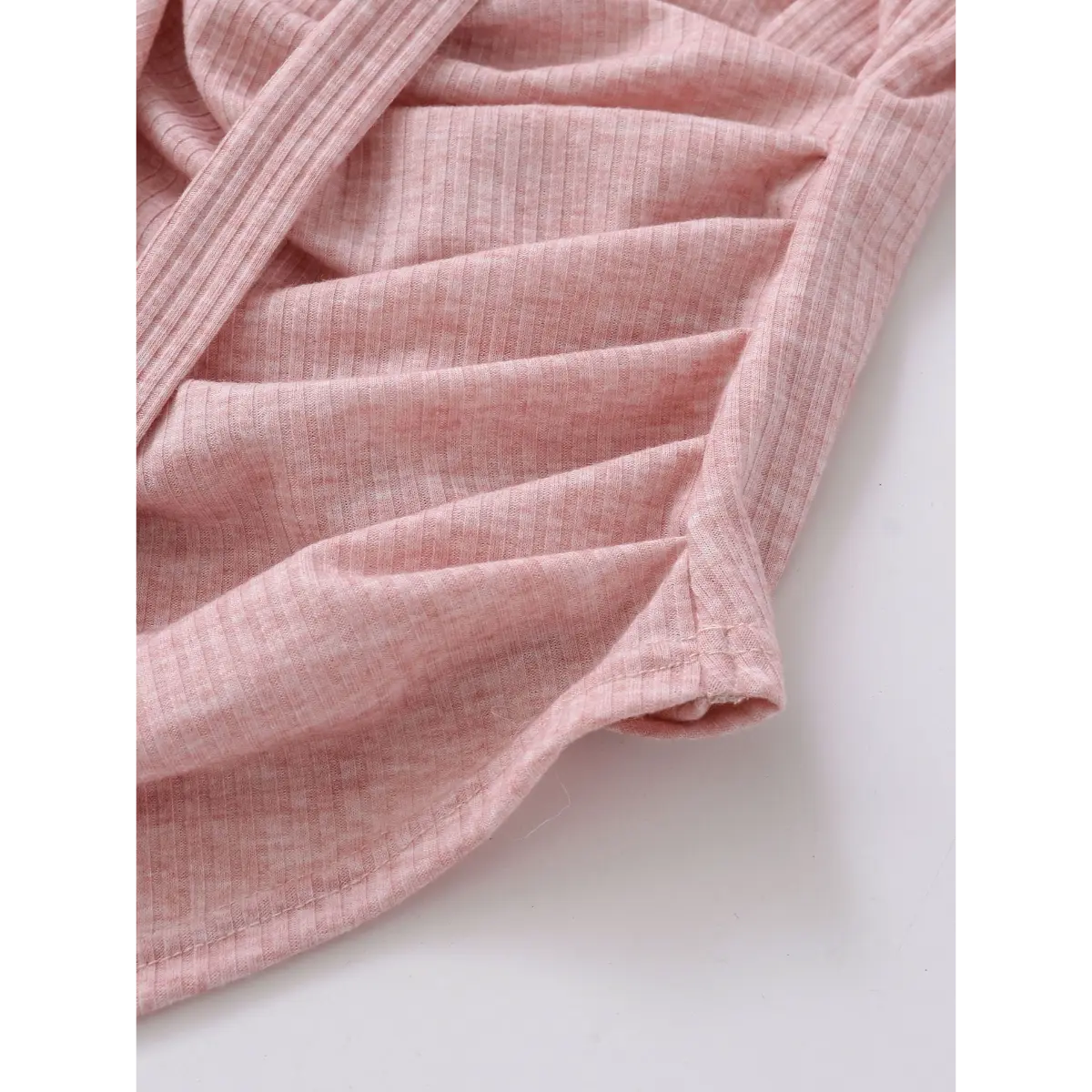 Close-up of the side ruching and hem on a pink ribbed halter wrap top, showing the texture and stitching.