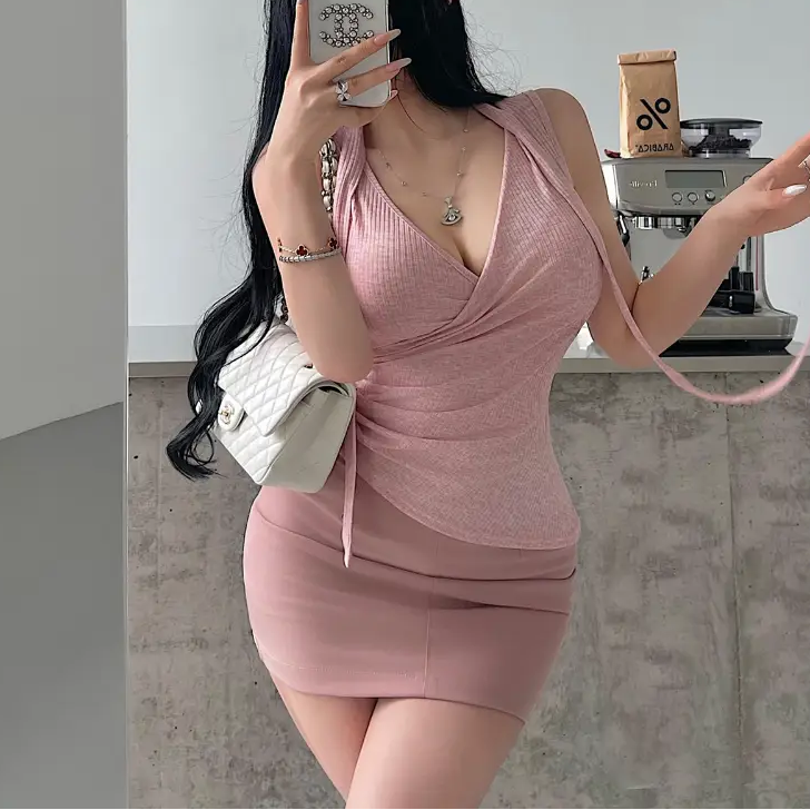 A woman wearing a pink ribbed halter wrap top with a tie detail, styled with a matching mini skirt and headband, taking a mirror selfie.