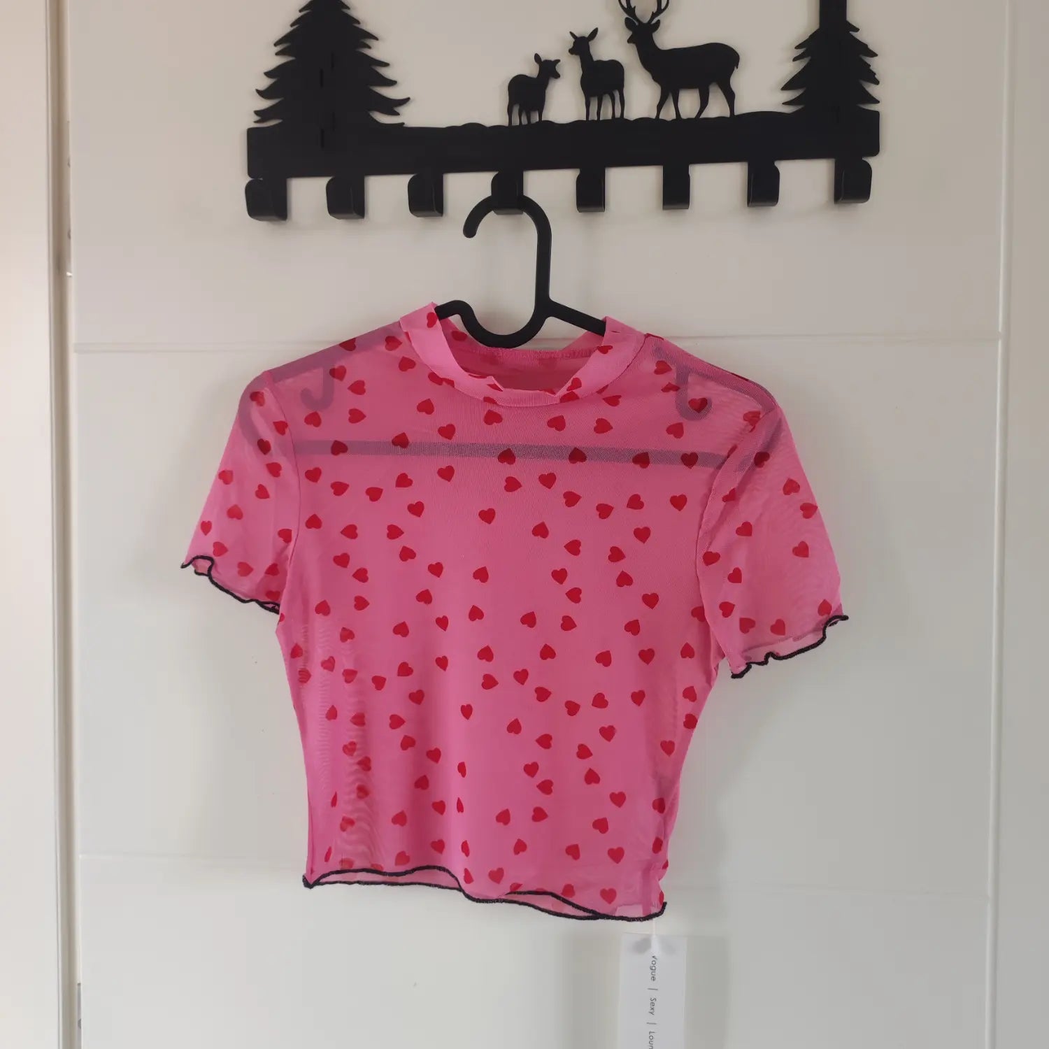 Hanging front view pink high neck sheer mesh top red heart print black ruffle trim on hanger