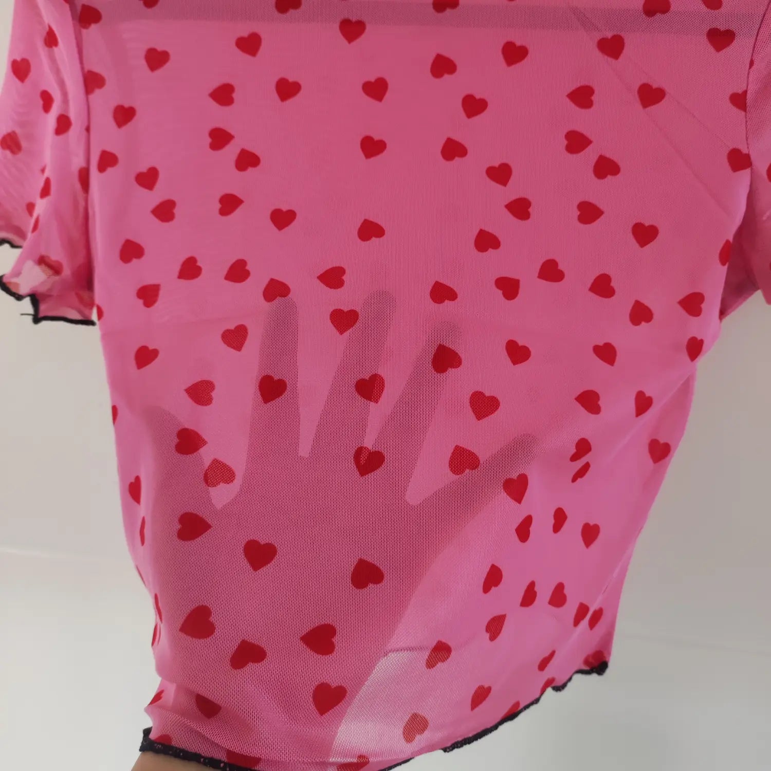 Close‑up transparency test sheer mesh fabric of pink top with red heart allover print