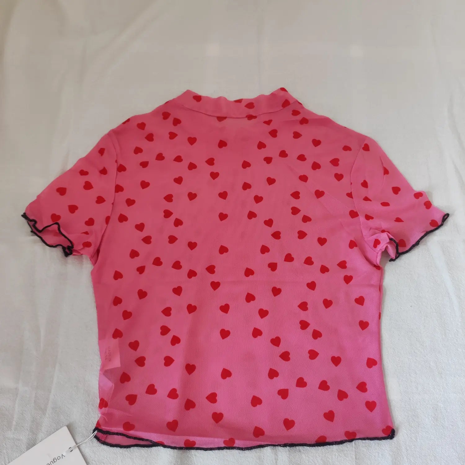 Flat lay back view pink sheer mesh short sleeve top with all over red heart print and black lettuce hem