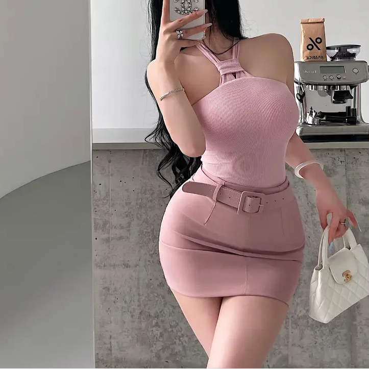 A woman wearing a pink ribbed keyhole halter top, styled with a matching belted mini skirt, taking a mirror selfie.