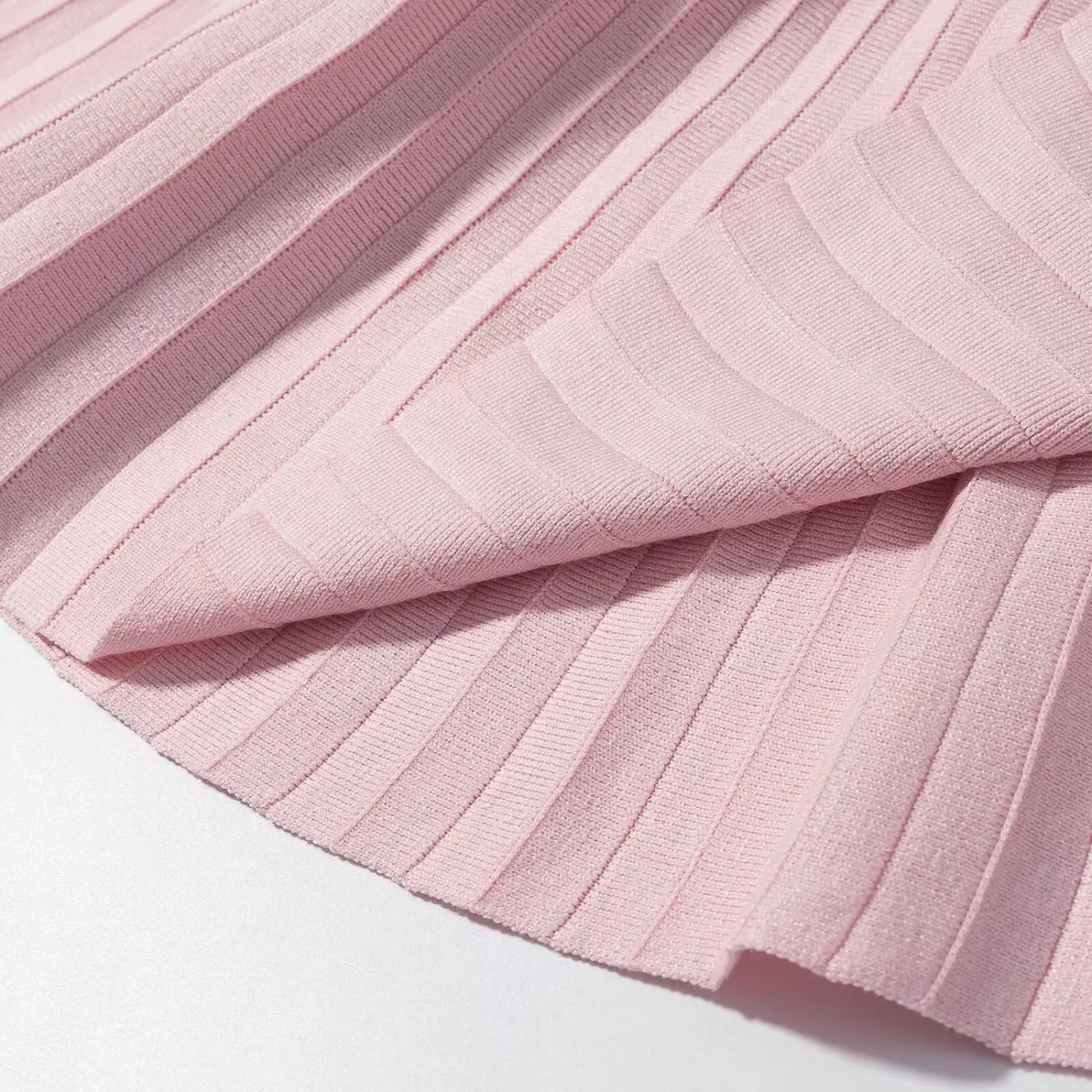 Close‑up folded fabric shot of pink ribbed knit pleated skirt, showing pleat construction and soft knit texture