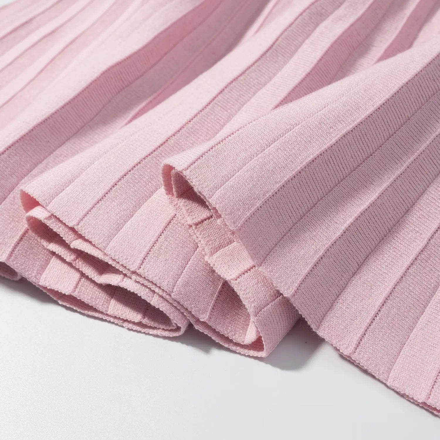 Close‑up folded hem detail of pink ribbed knit pleated mini skirt, showing fabric thickness and stitching