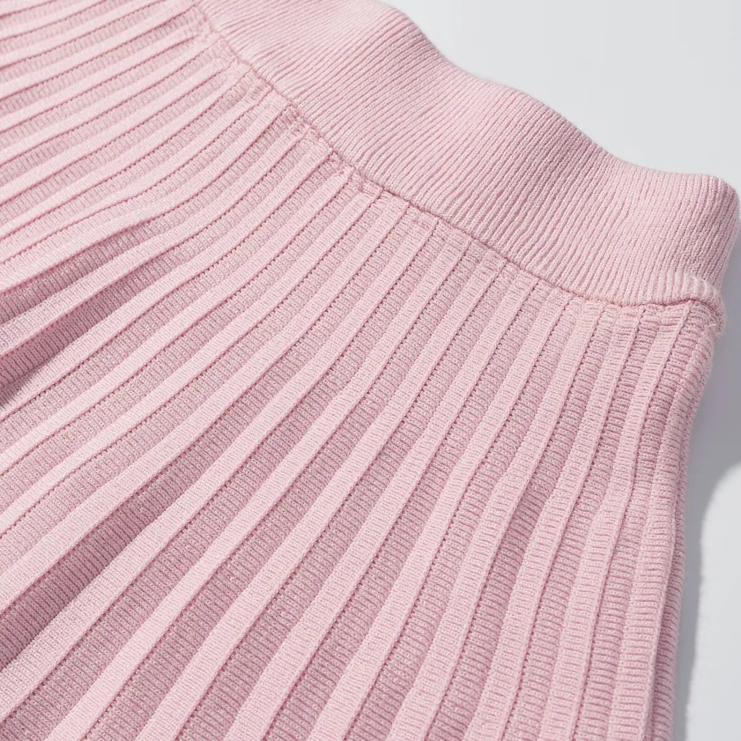 Close‑up seam detail of pink knit pleated mini skirt, wide ribbed waistband attaching to vertical pleated body