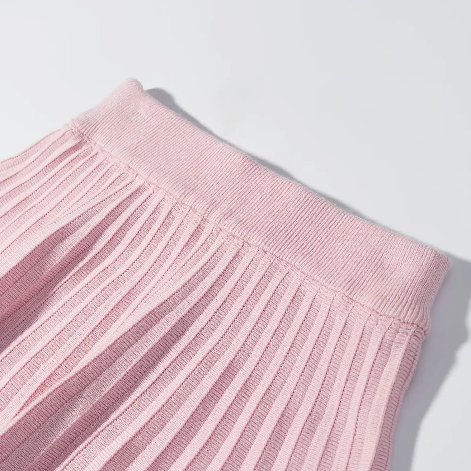 Close‑up of wide ribbed knit waistband on pink pleated mini skirt, seam and fabric texture detail