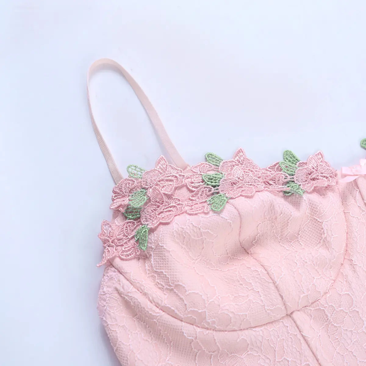 Close-up of the bustier-style top, showing the pink lace fabric, spaghetti strap, and floral appliqué with green leaves
