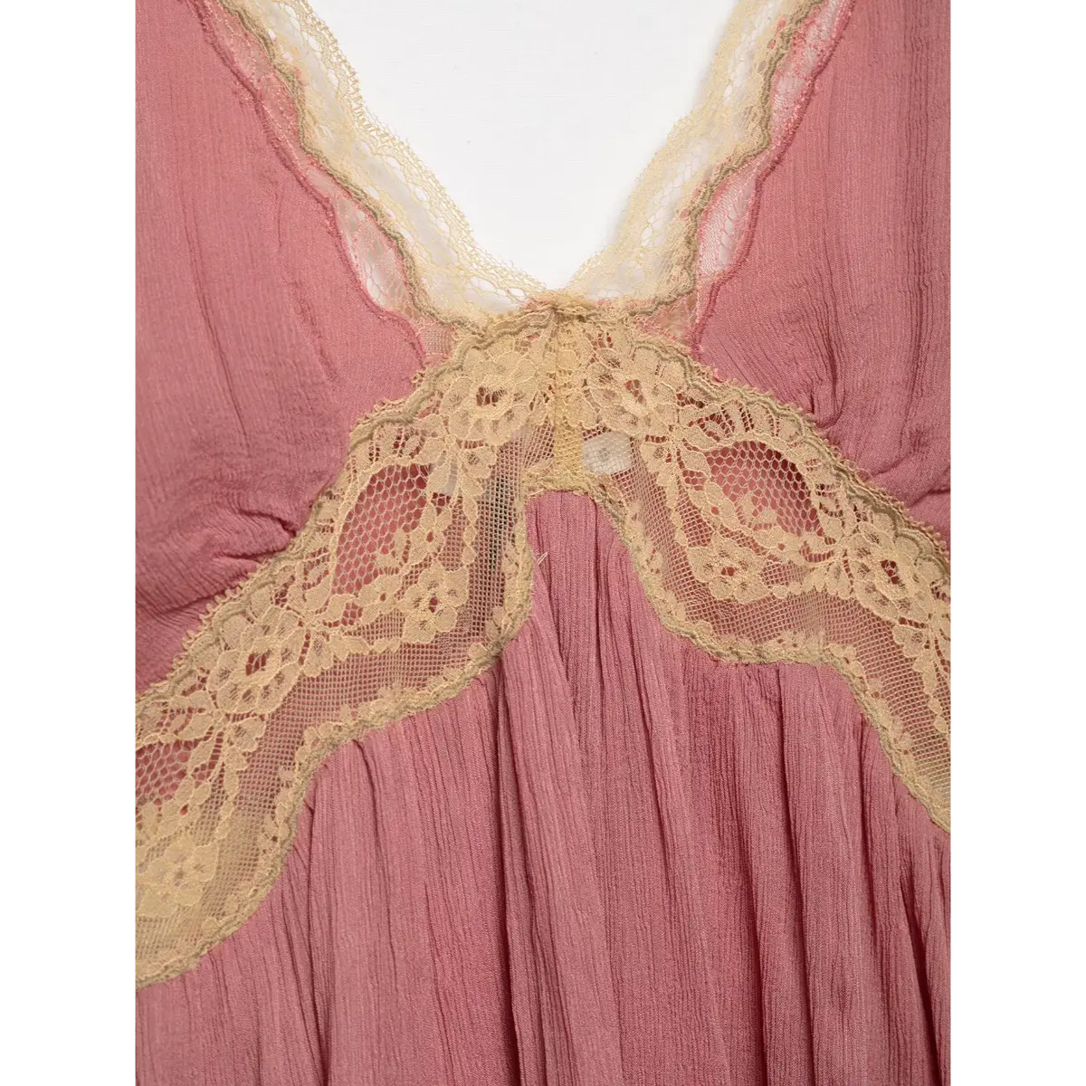 Close-up of the V-neckline and central lace panel on a pink peplum cami top, showing the button detail.
