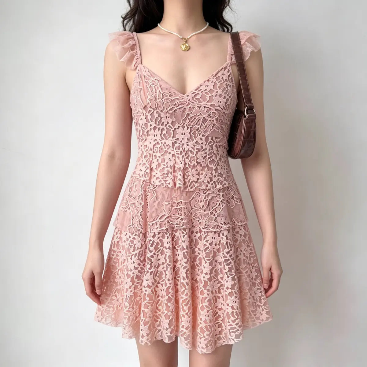 Model wearing a pink lace mini dress with tiered ruffled layers and ruffled straps, carrying a brown handbag.