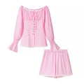 Full set flat lay main shot, baby pink off-shoulder long sleeve top + matching shorts, white lace hem trim, front heart metal buttons