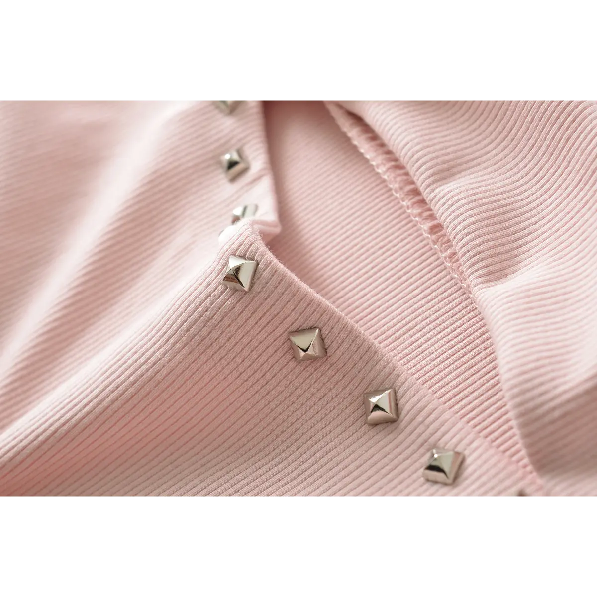 Close-up of the pyramid stud details on the neckline of a pink ribbed off-shoulder dress.
